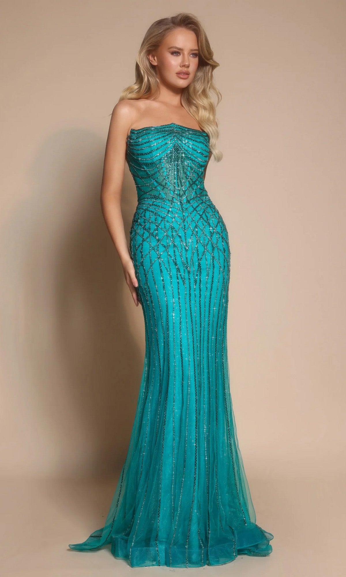 A woman with long, wavy blonde hair poses against a beige backdrop in the Portia and Scarlett PS26130 Long Formal Dress in Peacock, featuring a strapless fitted silhouette with sequin details.